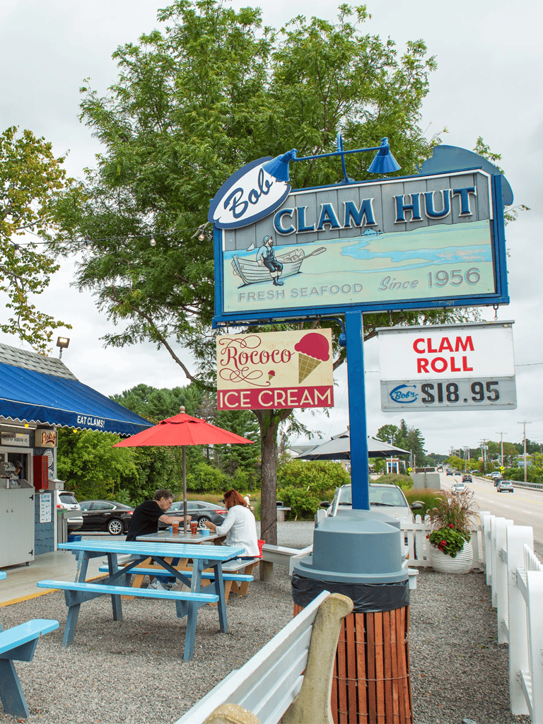 Clam Hut seafood restaurant sign with outdoor seating and ice cream, located on a busy roadside.