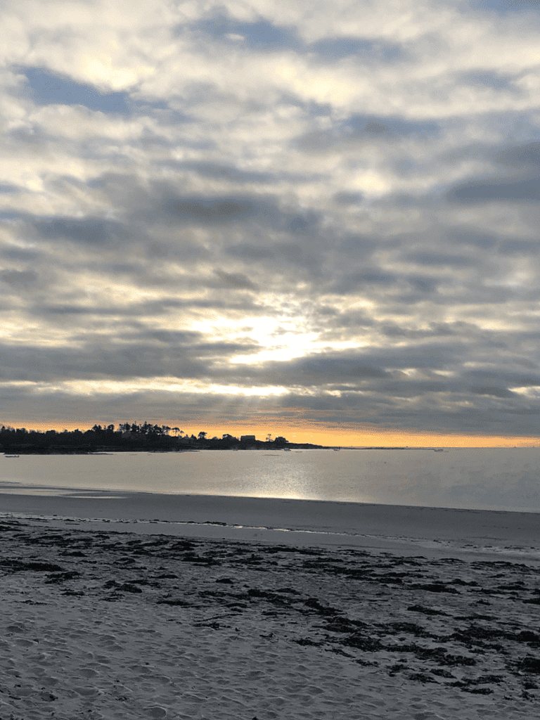 Tranquil beach scene during sunset with cloudy sky and calm waters.