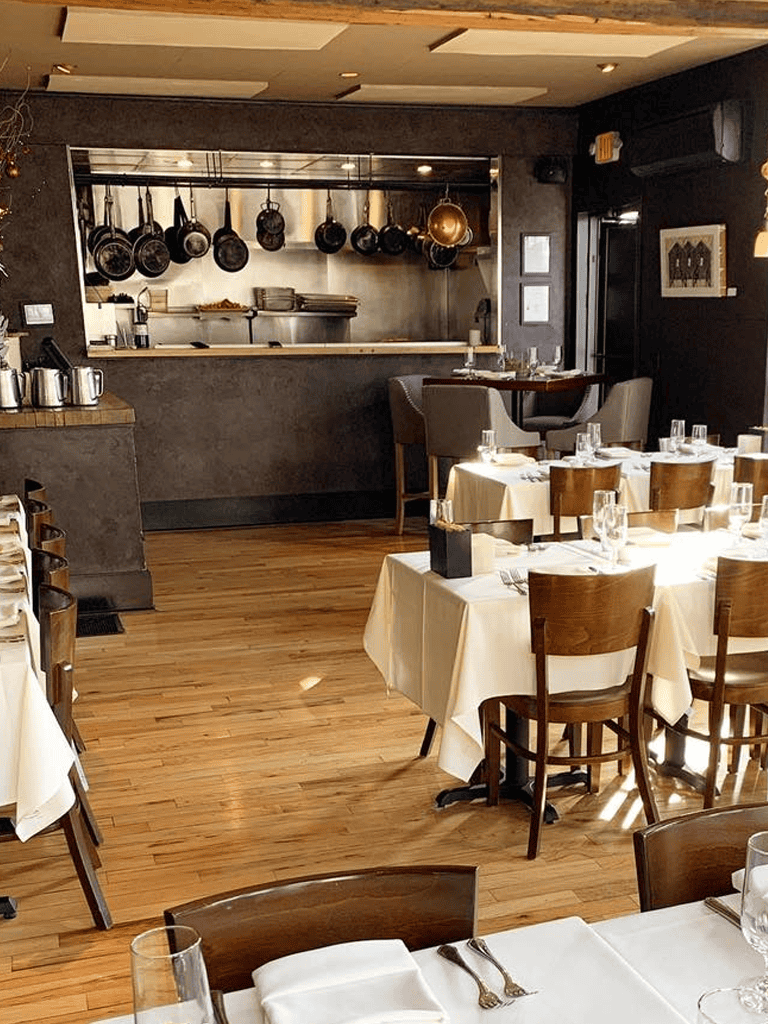 Elegant restaurant dining area with white tablecloths and open kitchen in the background, inviting for fine dining.