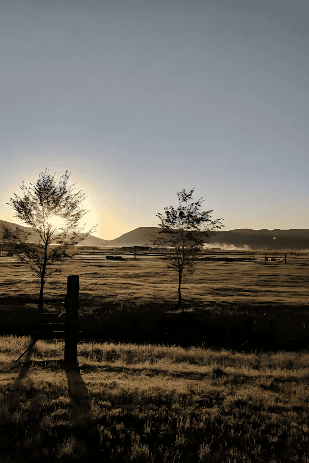 Serene sunrise over rural farmland with trees and mountains, showcasing scenic outdoor destinations by QuestForDirections.