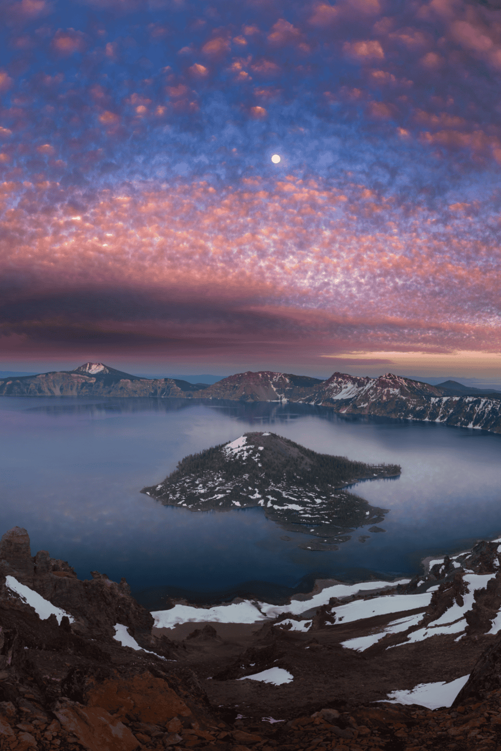Vibrant sunrise over Crater Lake with colorful sky, Mount Mazama, and surrounding volcanic landscape.