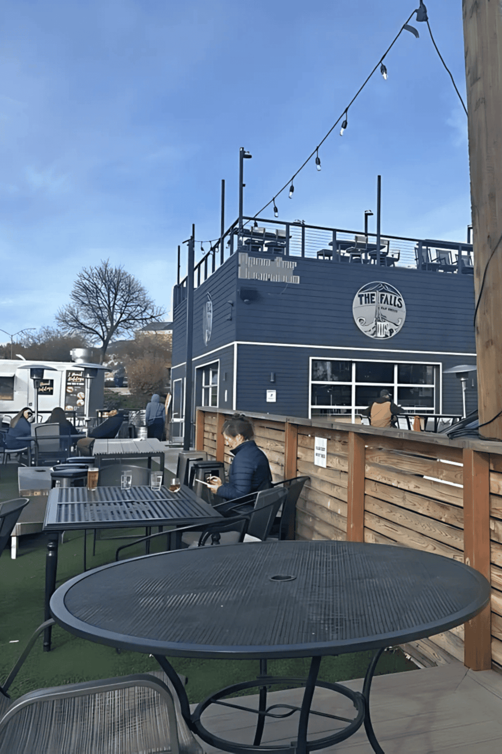 Outdoor restaurant patio at The Falls bar with seating, string lights, and people enjoying the view.