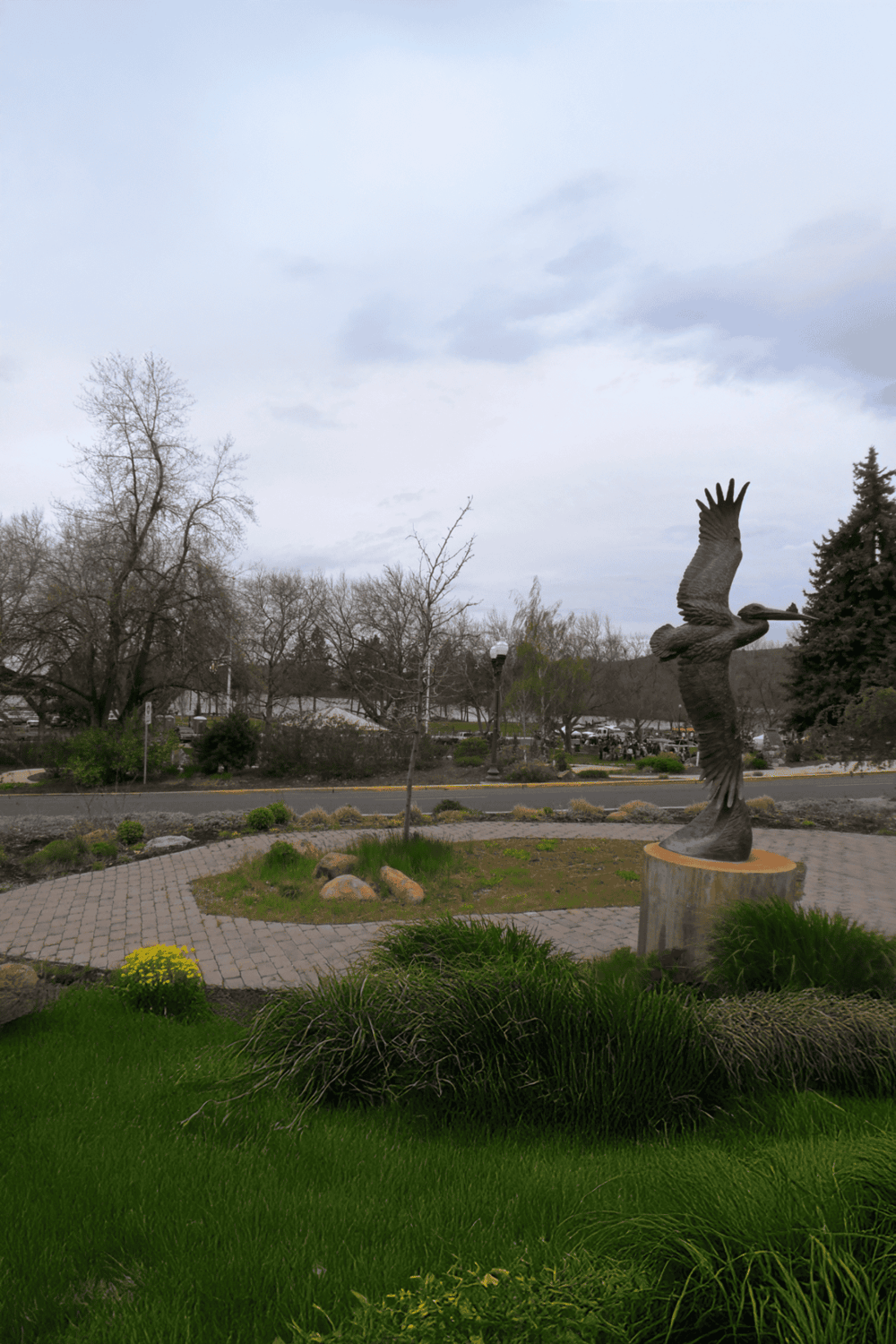 Colorful street sculpture of a flying bird at a park with trees and greenery.