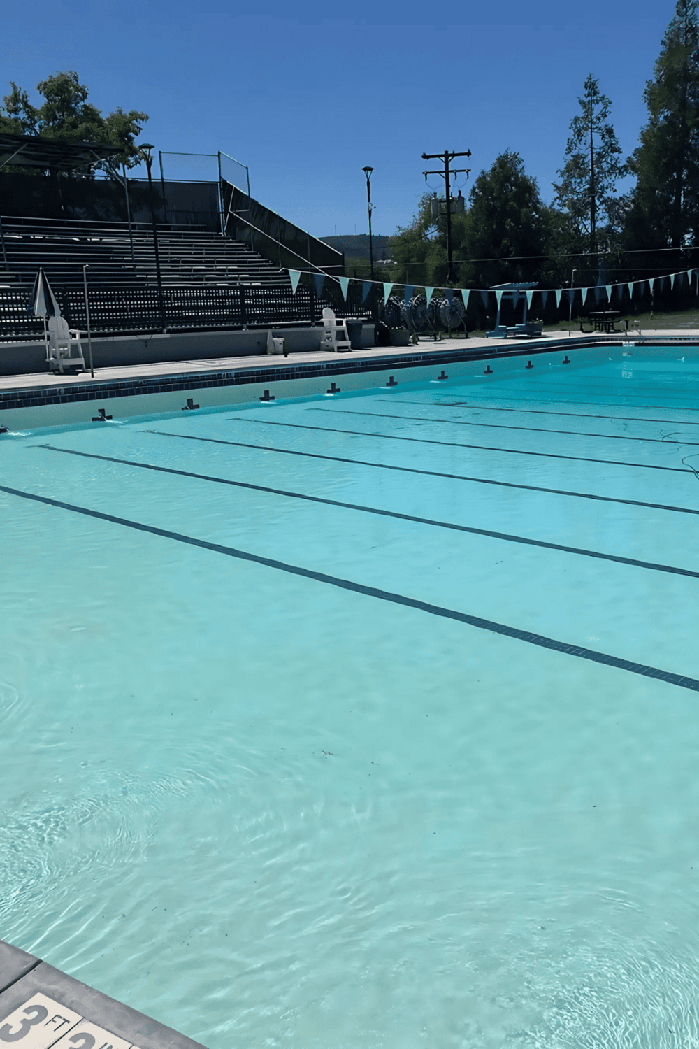 Clean outdoor swimming pool with clear water, bleachers, and scenic mountain backdrop.