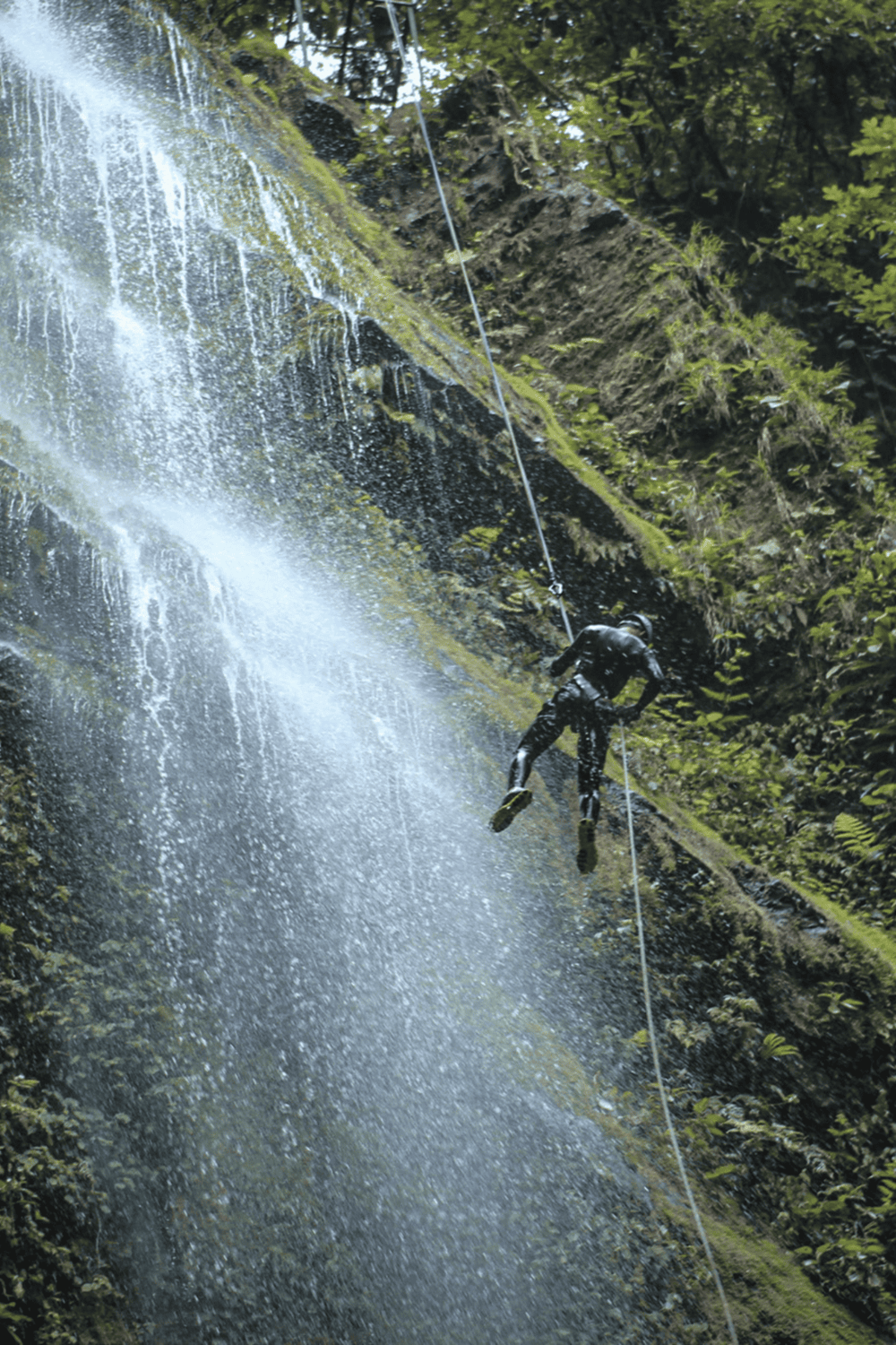 Rappelling down a lush waterfall in an adventure outdoor activity.
