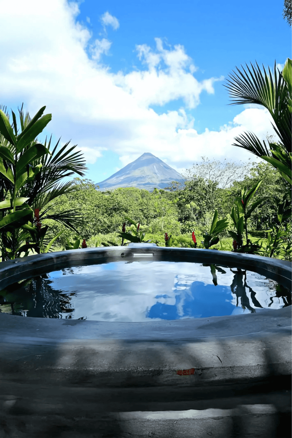 Lush tropical scenery with a hot tub in the foreground and a scenic volcano view in the background.