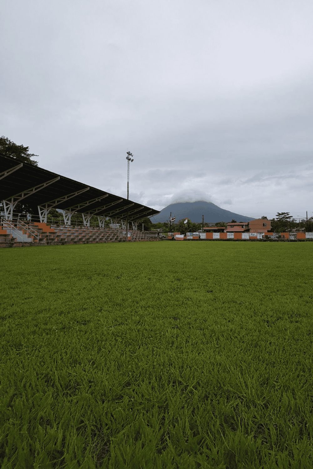 Open-air football stadium with green field and mountain view, perfect for sports events and outdoor activities.