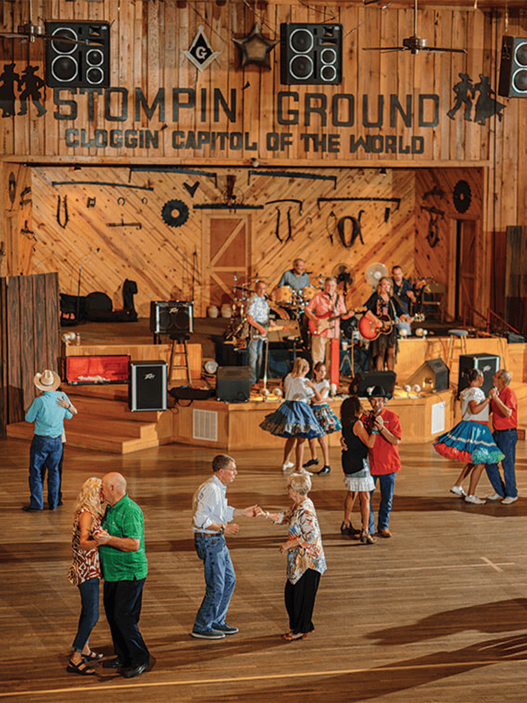 Live country dance event with live band at rustic wooden venue, couples and groups dancing, colorful outfits, and lively atmosphere.