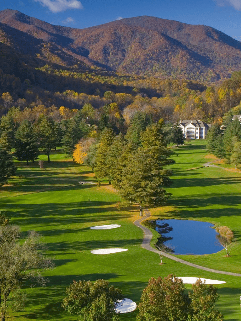 Vast golf course with water hazards and mountain backdrop in fall season.