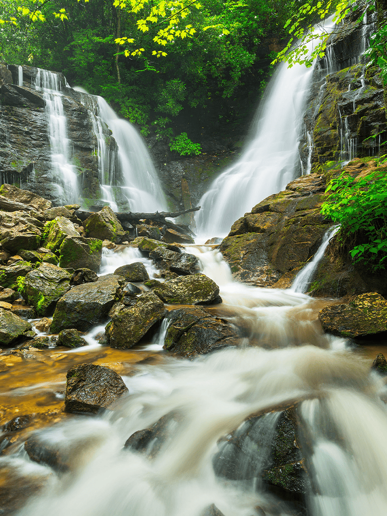 Vibrant waterfall cascading over rocks in lush green forest with flowing stream.