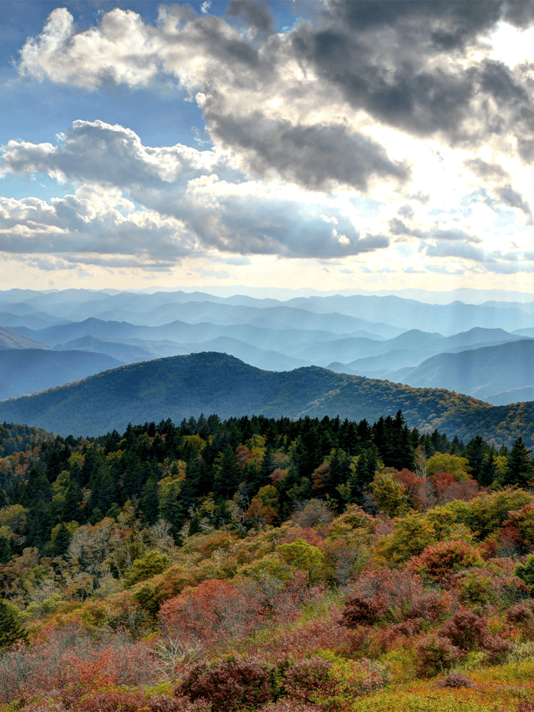 Vast mountain range with colorful autumn foliage and dramatic cloudy sky.