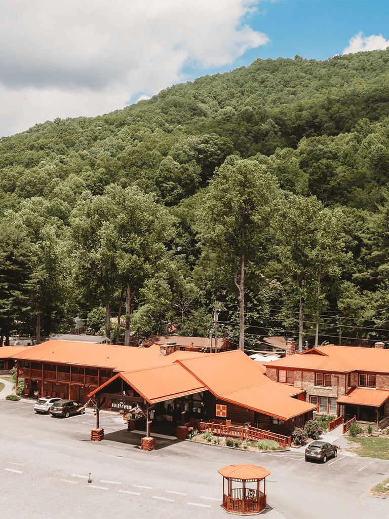 Cozy mountain lodge with red roof and parking lot, nestled near lush green forest and scenic mountain views.