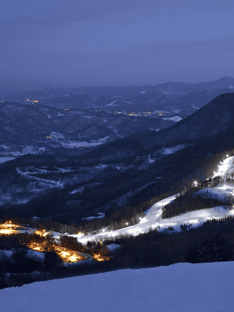 Night mountain landscape with snow-covered slopes and illuminated ski trails, scenic winter resort area.