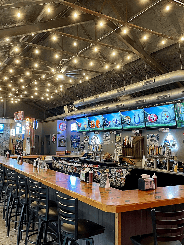 Cozy sports bar with multiple TV screens, illuminated string lights, and a lively atmosphere for watching games.