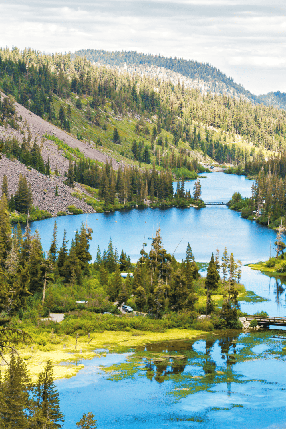 Serene mountain lake surrounded by lush pine trees and forested hillsides, scenic outdoor destination.