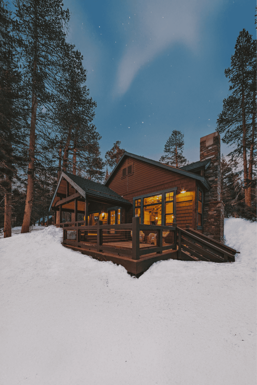 Cozy mountain cabin in snow-covered forest with warm interior lights, ideal for winter getaway.