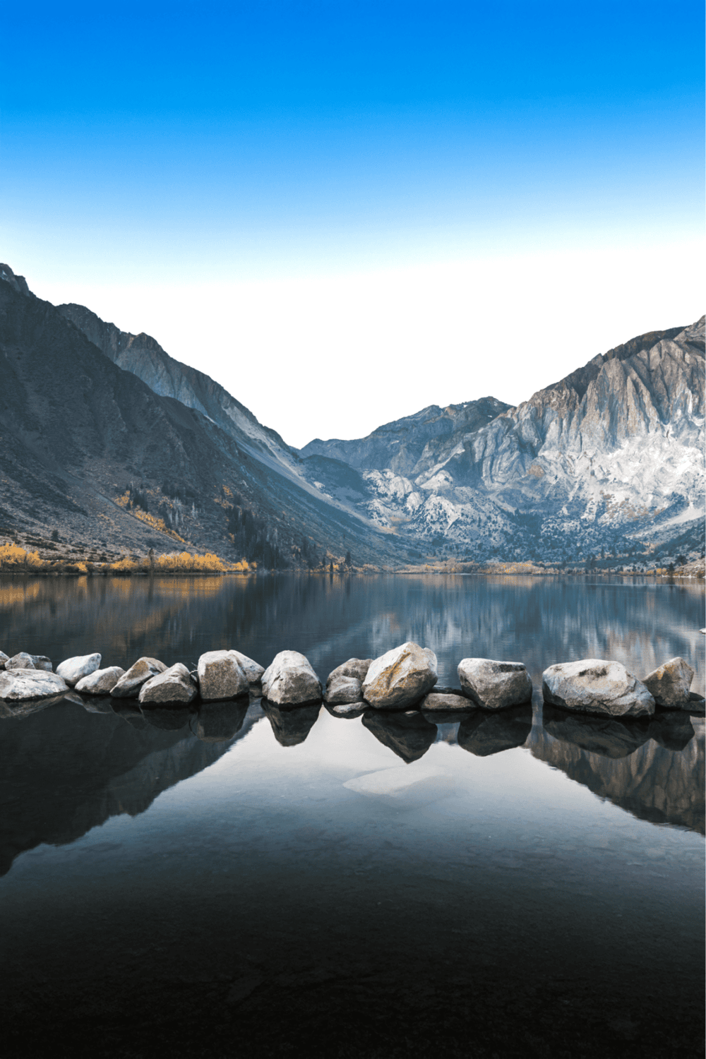 Serene mountain lake with clear water reflecting surrounding peaks and sky.