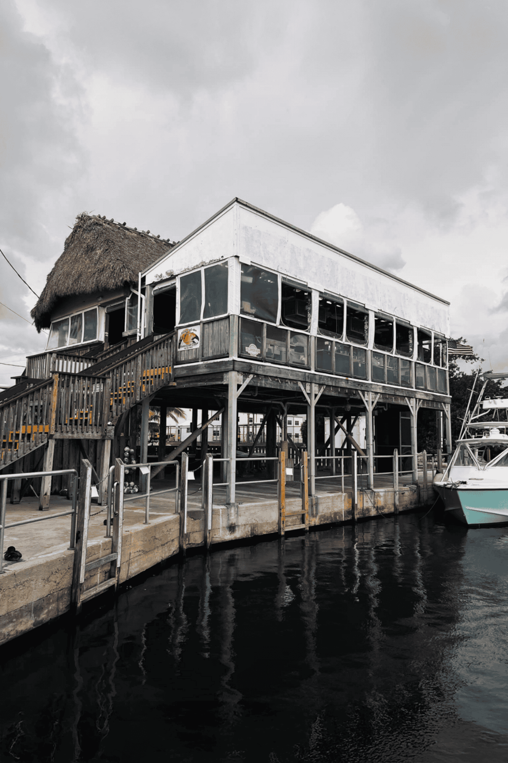 Historic waterfront restaurant on stilts with boat dock in a marina setting.