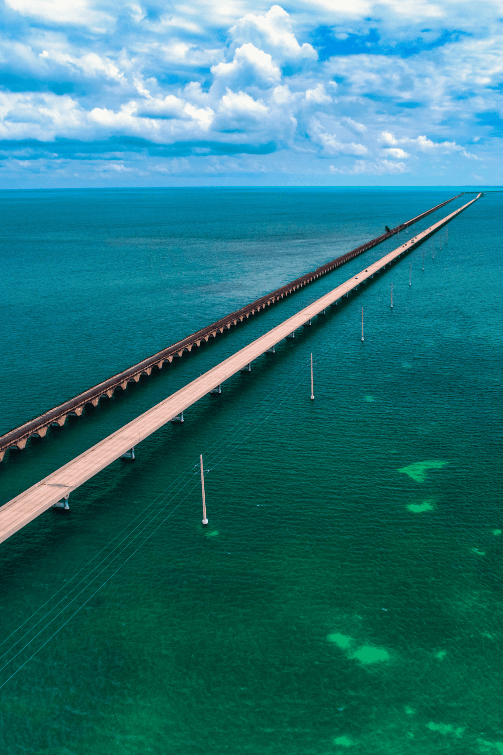 Long bridge crossing the ocean with clear blue skies and scattered clouds.