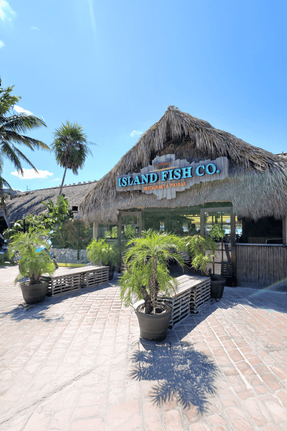 Colorful tropical restaurant exterior with tiki bar, palm trees, and lush greenery.