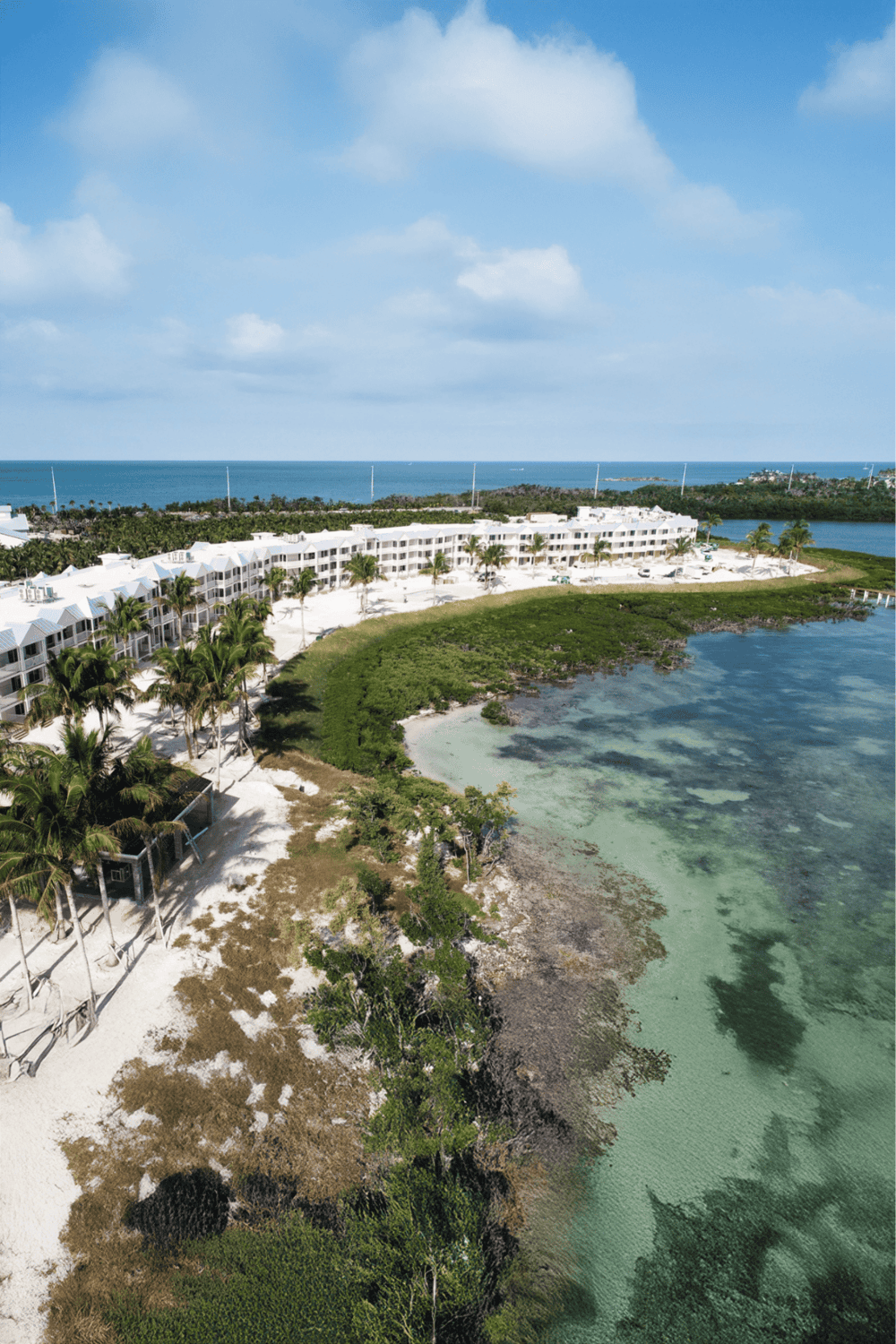 Aerial view of a beachfront resort with white buildings, palm trees, and clear turquoise water at QuestForDirections.