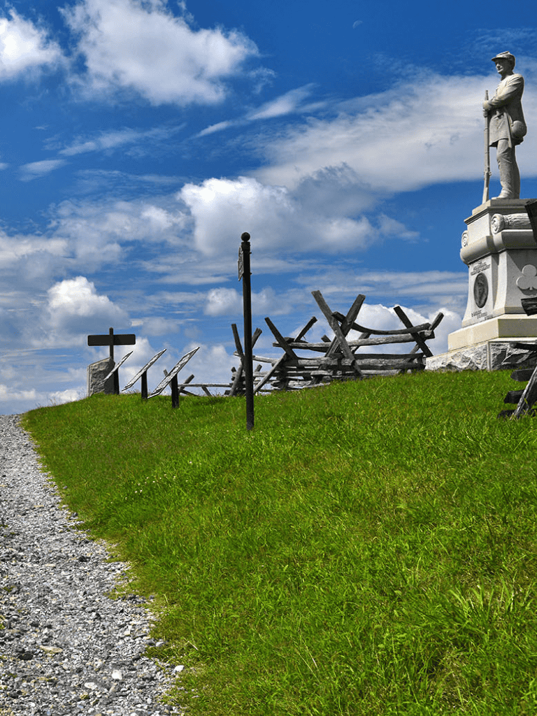 Ancient war memorial statue on grassy hill with cloudy sky background, historical landmark and outdoor site.