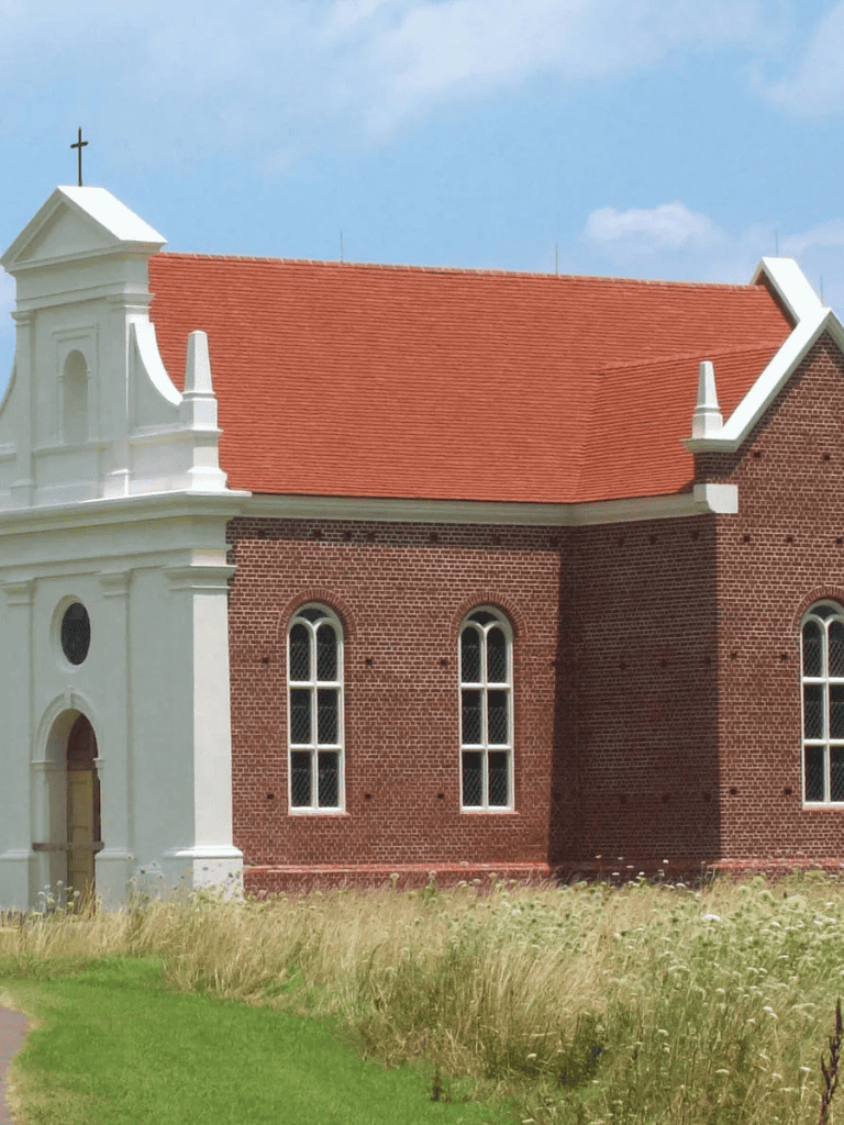Small white chapel with red brick walls and arched windows, rural church in a scenic landscape.