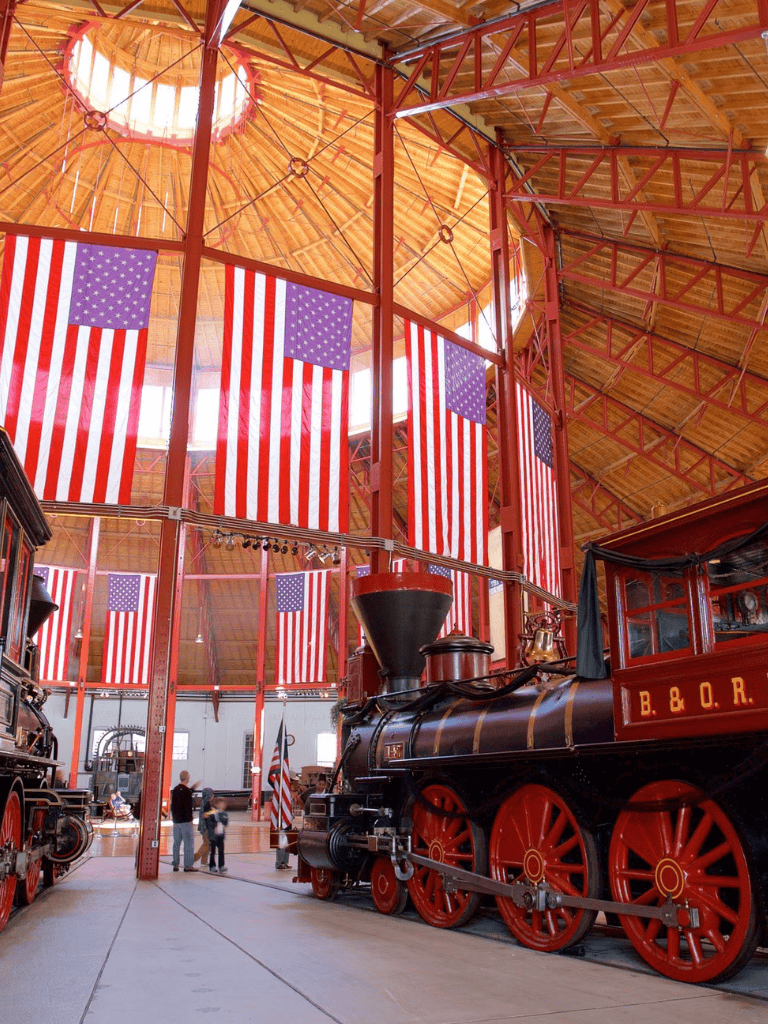 American flags displayed inside a train museum with vintage steam locomotives.