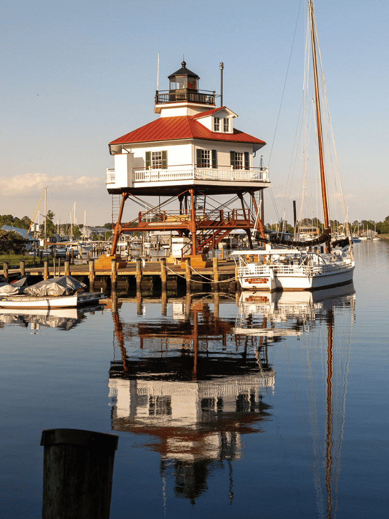 Lighthouse boat house at the marina, picturesque waterfront scene with sailboats and dock area.