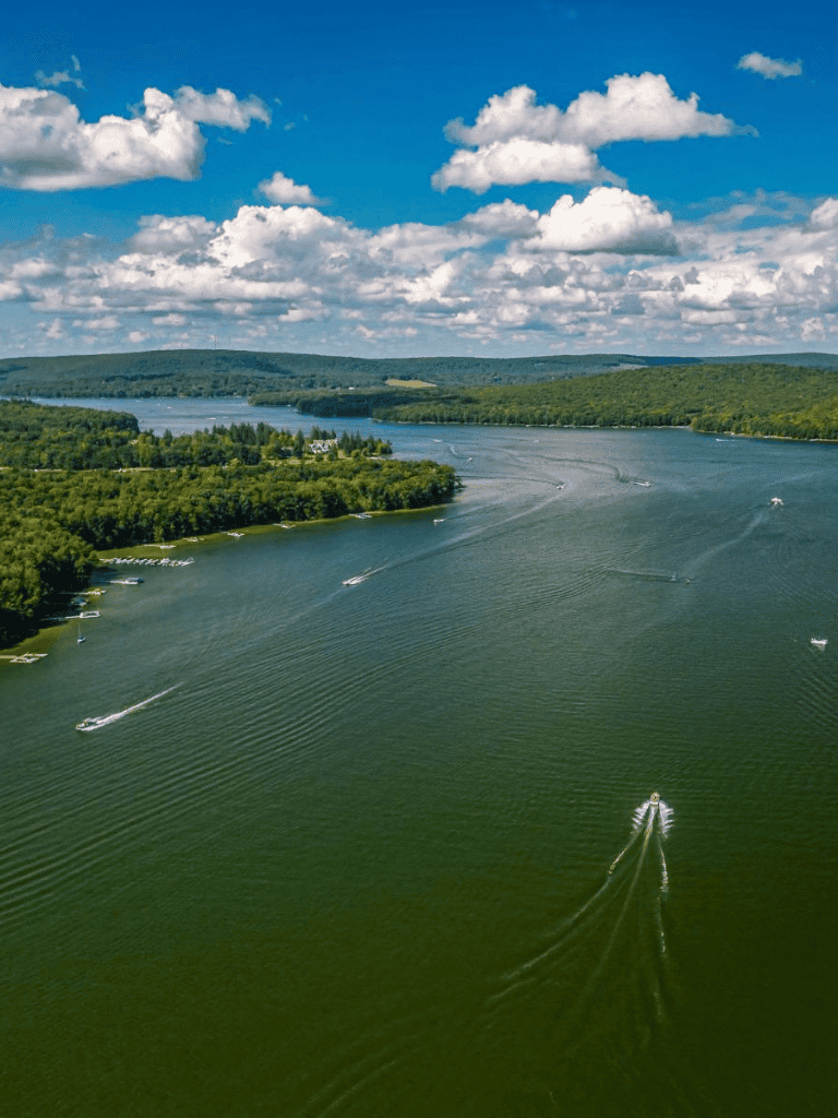 Boats on a winding river with lush green hills and a cloudy sky in the background.