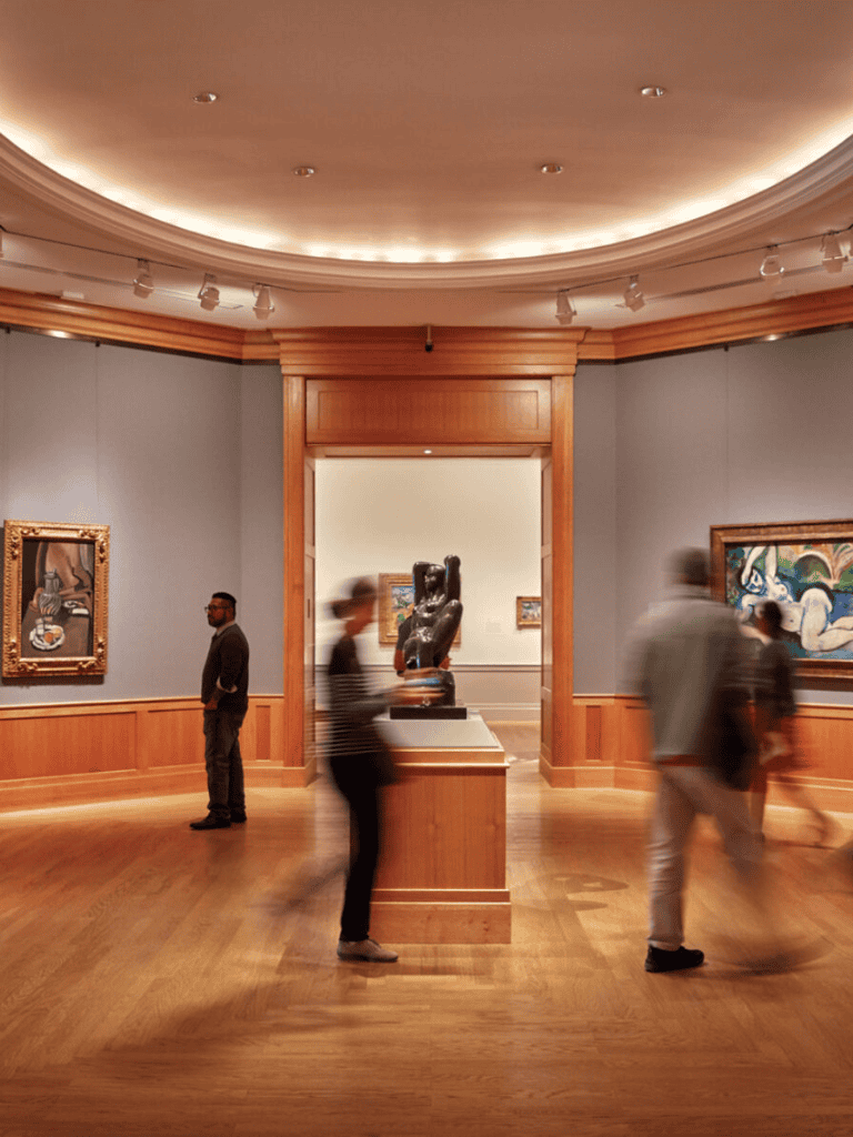 History museum art gallery, visitors viewing sculptures and paintings, wooden flooring, soft lighting, cultural experience.