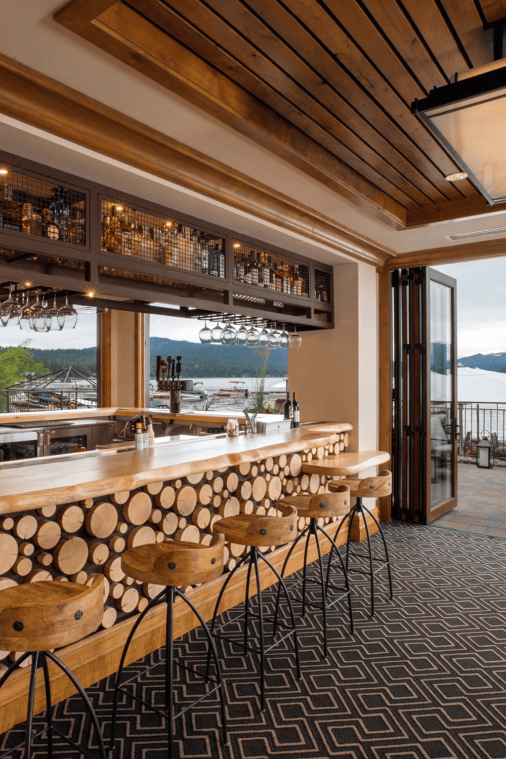 Cozy waterfront bar with wood accents, overlooking a lake and mountains, perfect for relaxing and enjoying drinks.