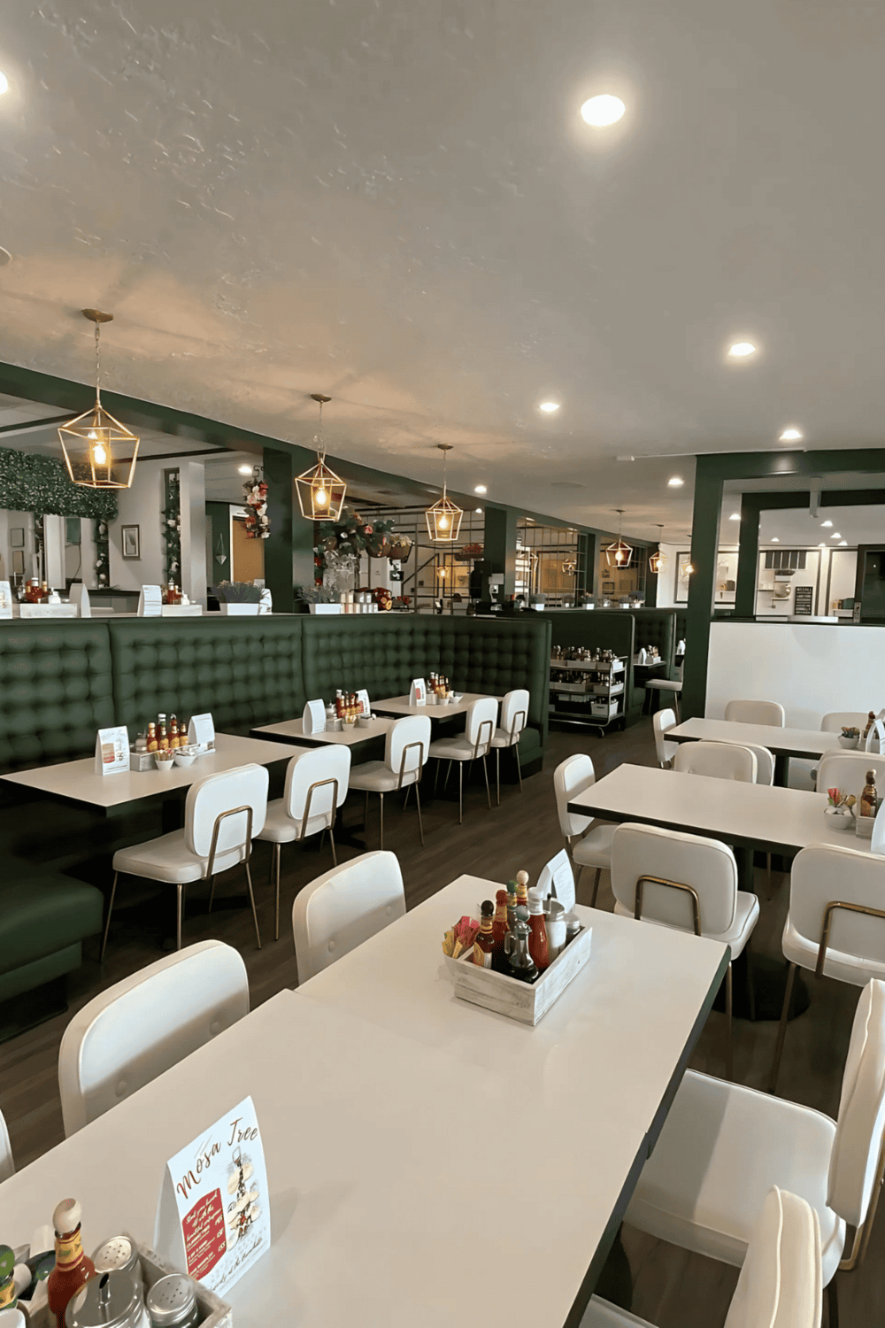 Cozy modern restaurant interior with white tables, green seating, and decorative lighting.