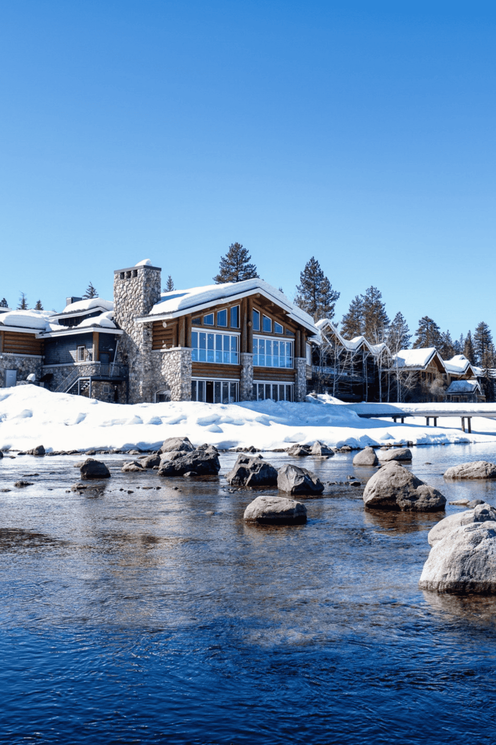 Snowy mountain retreat with large windows and a river in front, perfect for remote work and relaxation.