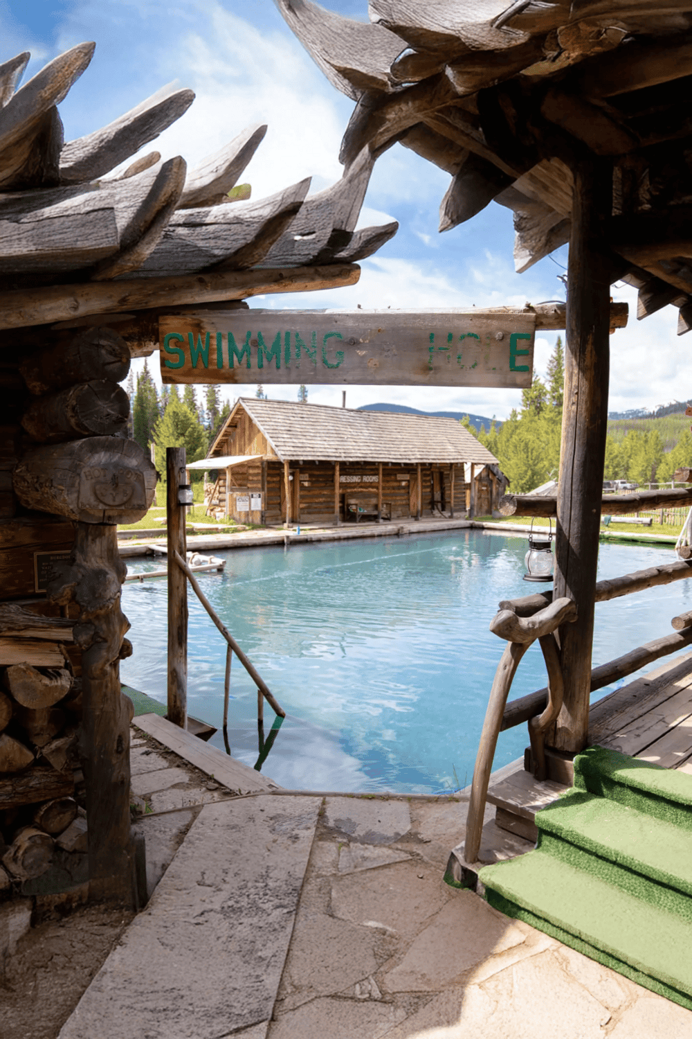 Relaxing swimming hole at rustic lodge with wooden structures and mountain view in the background.