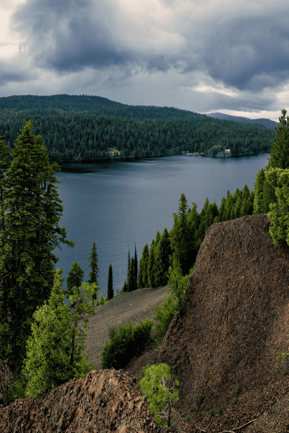 Serene lake surrounded by lush green pine forests and rugged volcanic rocks under cloudy sky.