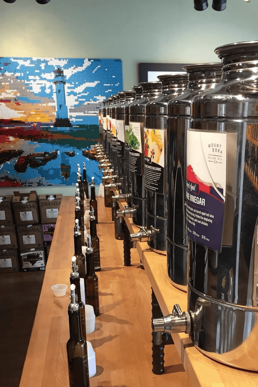 Fresh olive oil bottles display at QuestForDirections store, with colorful mosaic art in the background.