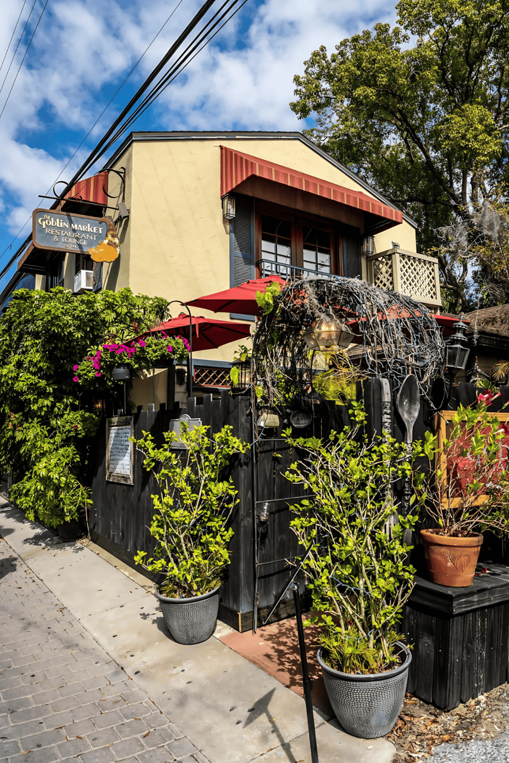 Charming restaurant exterior with lush greenery, outdoor seating, and a cozy ambiance, ideal for dining in a vibrant neighborhood.