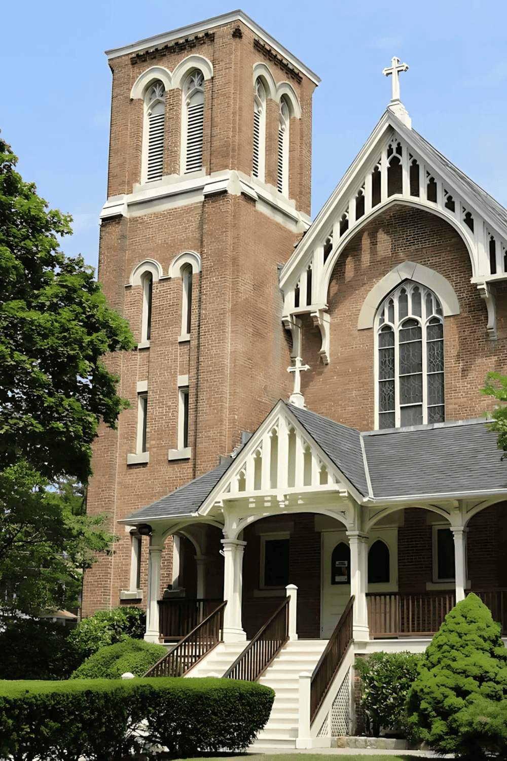 Victorian church with tall steeple and white trim, surrounded by lush greenery, located in a charming historic neighborhood.
