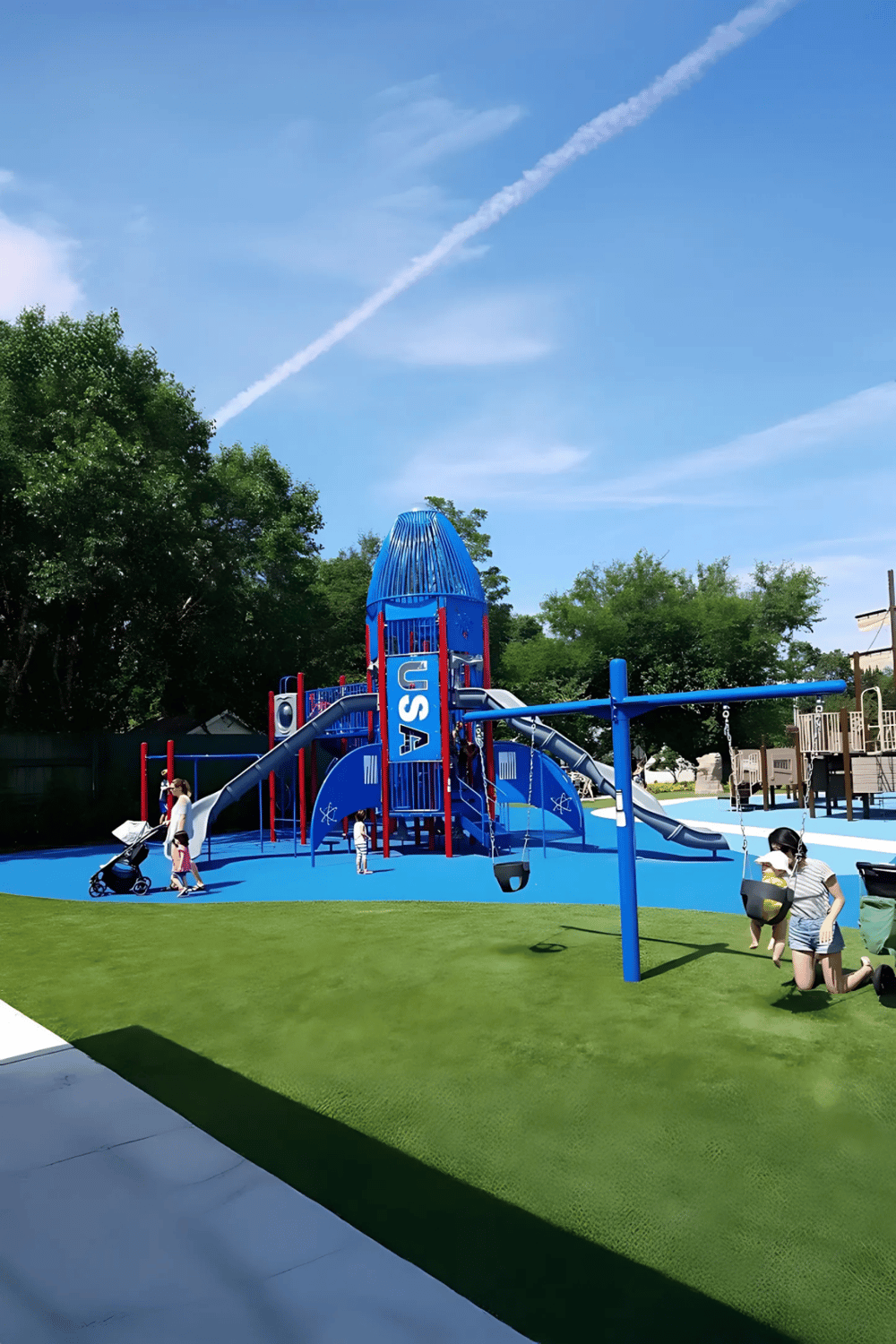 Colorful USA-themed playground with slides and swings for kids, surrounded by greenery and blue sky.