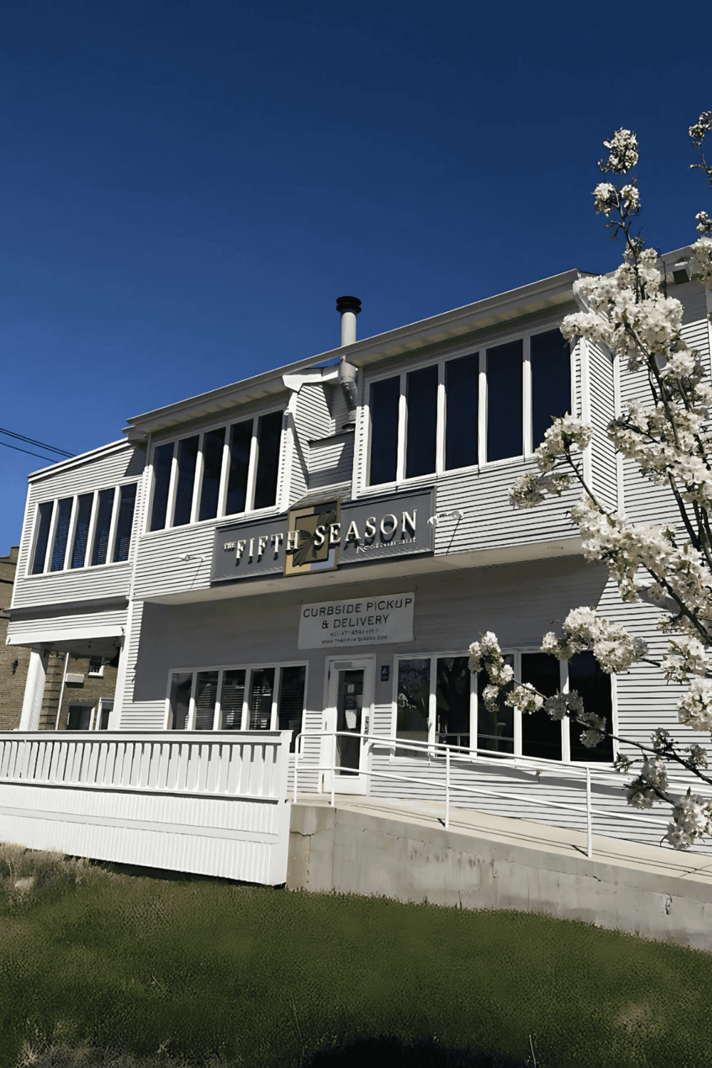 Cozy restaurant building with white siding, large windows, and a sign for The Fifth Season, under clear blue sky.