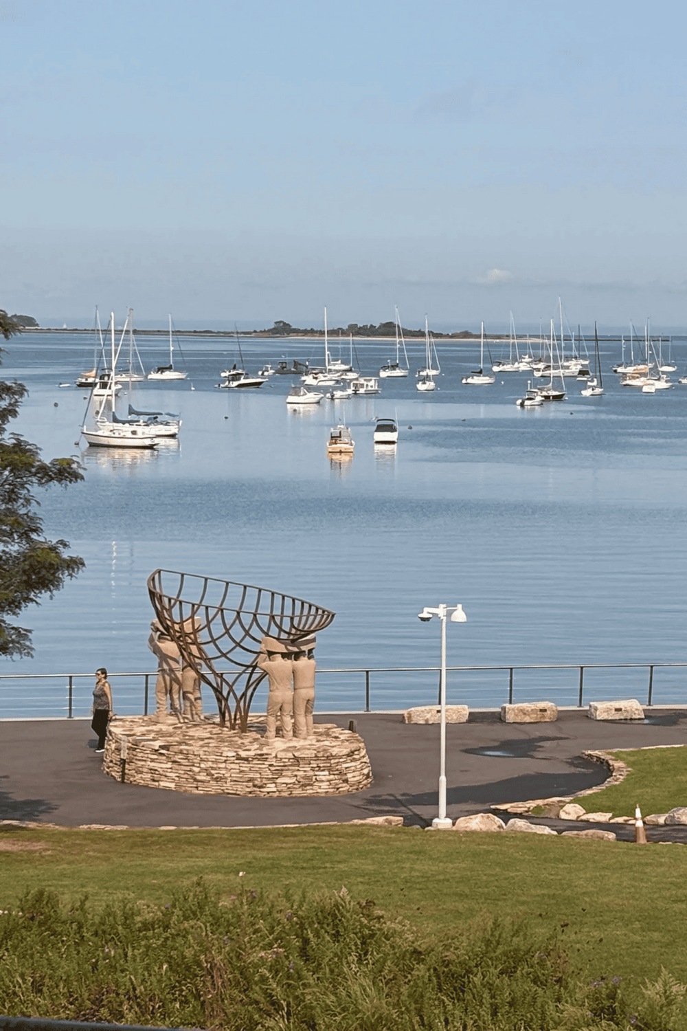 Boat marina with sailboats on calm water and a public art sculpture on a waterfront park.