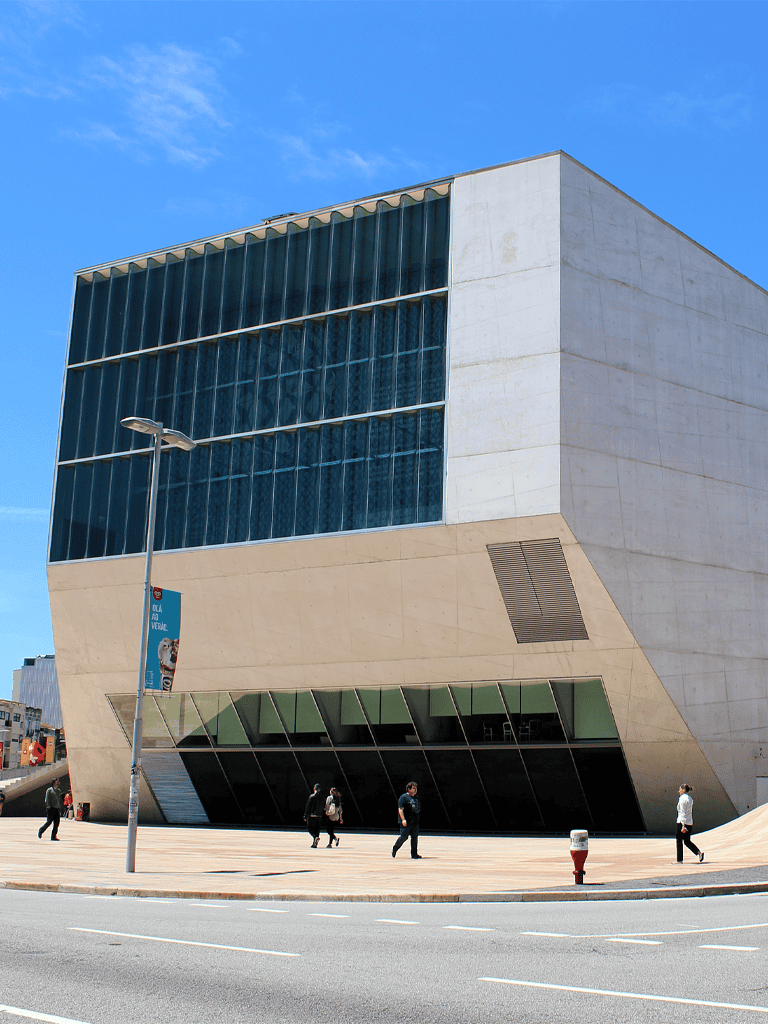 Modern university campus building with glass and concrete architecture, facing a busy street in daytime.