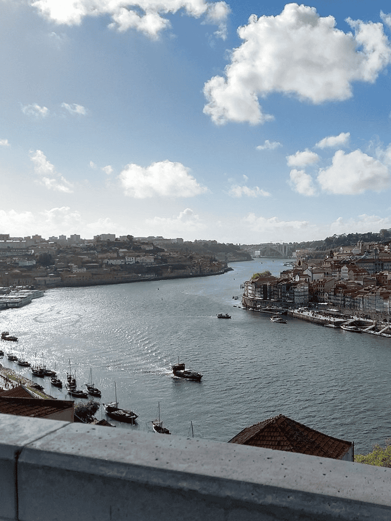 Scenic river view of Porto, Portugal with boats and colorful waterfront buildings, under a partly cloudy sky.