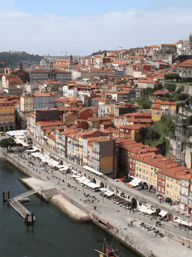 Colorful hillside Portuguese cityscape with riverfront promenade and restaurant terraces.