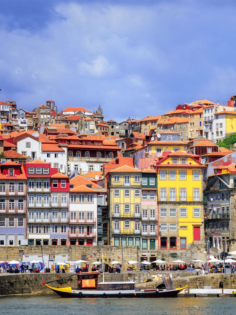 Colorful hillside houses in Porto, Portugal, with boats docked along the river, scenic coastal cityscape, vibrant neighborhood, Travel Portugal.