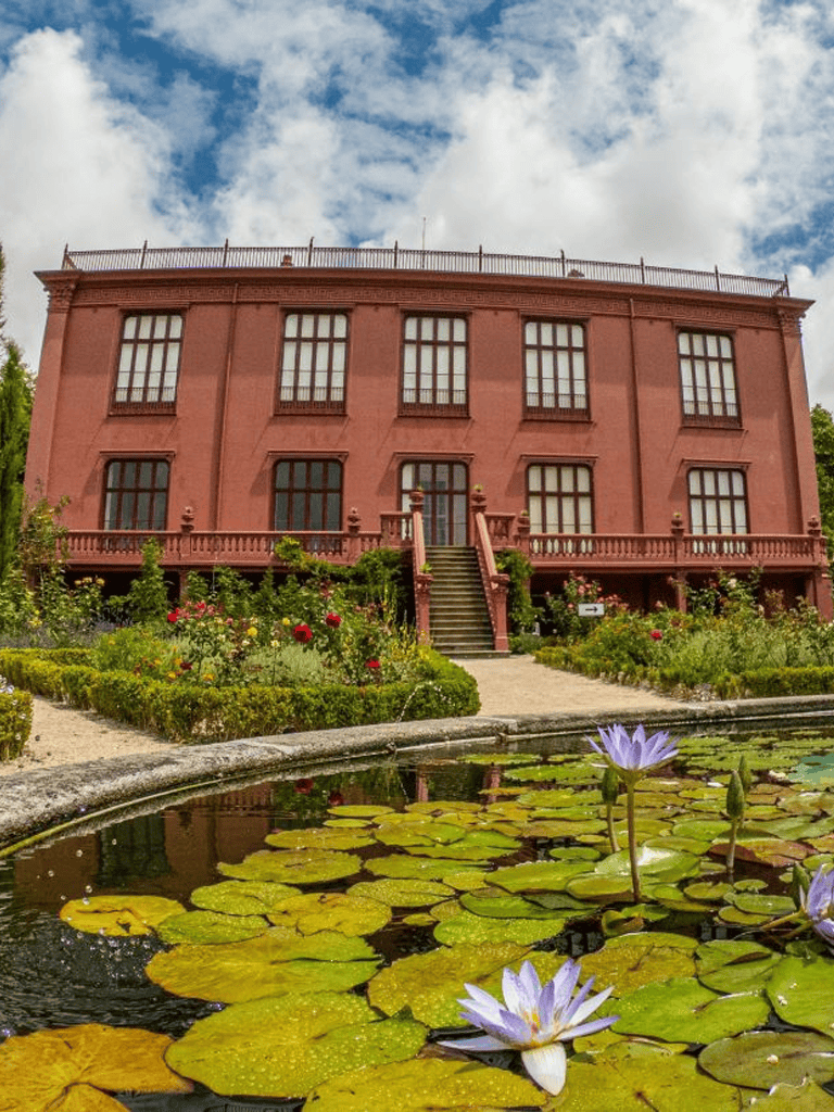 Elegant red historic house with garden and water lily pond, ideal for travel and sightseeing photography.