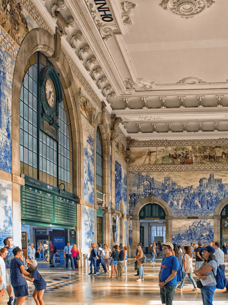 Elegant historic train station interior with travelers, ornate architecture, and blue tiled murals.