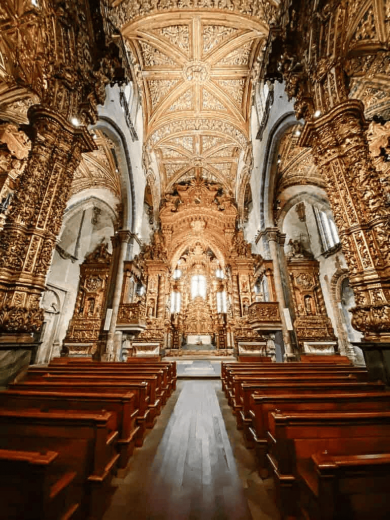 Intricate Baroque church interior with gold-leaf details, wooden pews, and ornate altar design.