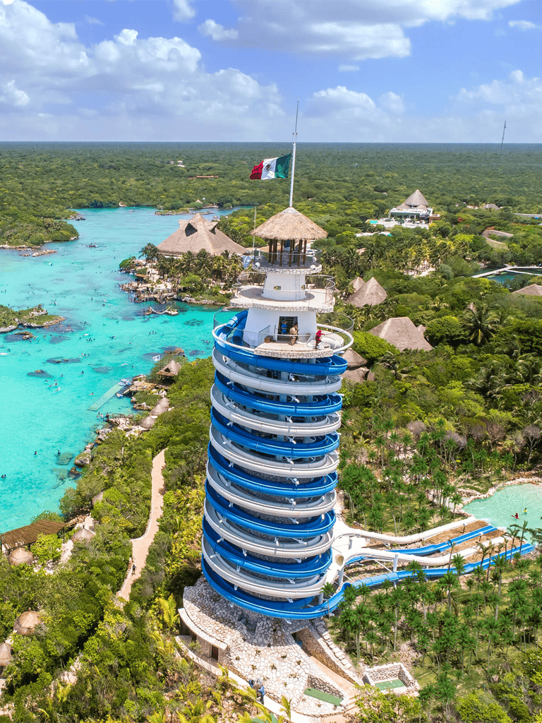Aqua thrill water slide tower in tropical resort with turquoise ocean and lush greenery.